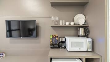 A kitchenette with a flat-screen TV, a coffee maker, a microwave, and a shelf with glasses and plates.