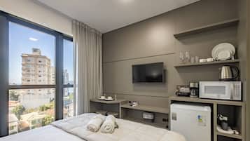 Habitación de hotel con cama, televisión, cafetera, microondas y vista de la ciudad.