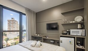 A hotel room with a bed, a TV, a coffee maker, a microwave, and a view of the city. - MHFBs Edifício Moderno piscina vista mar (Itapema)