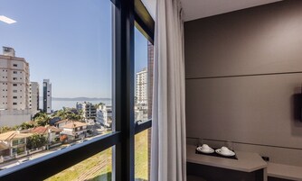 Habitación de hotel con un ventanal grande, vistas a la ciudad y una pequeña zona de estar con una mesa y sillas.