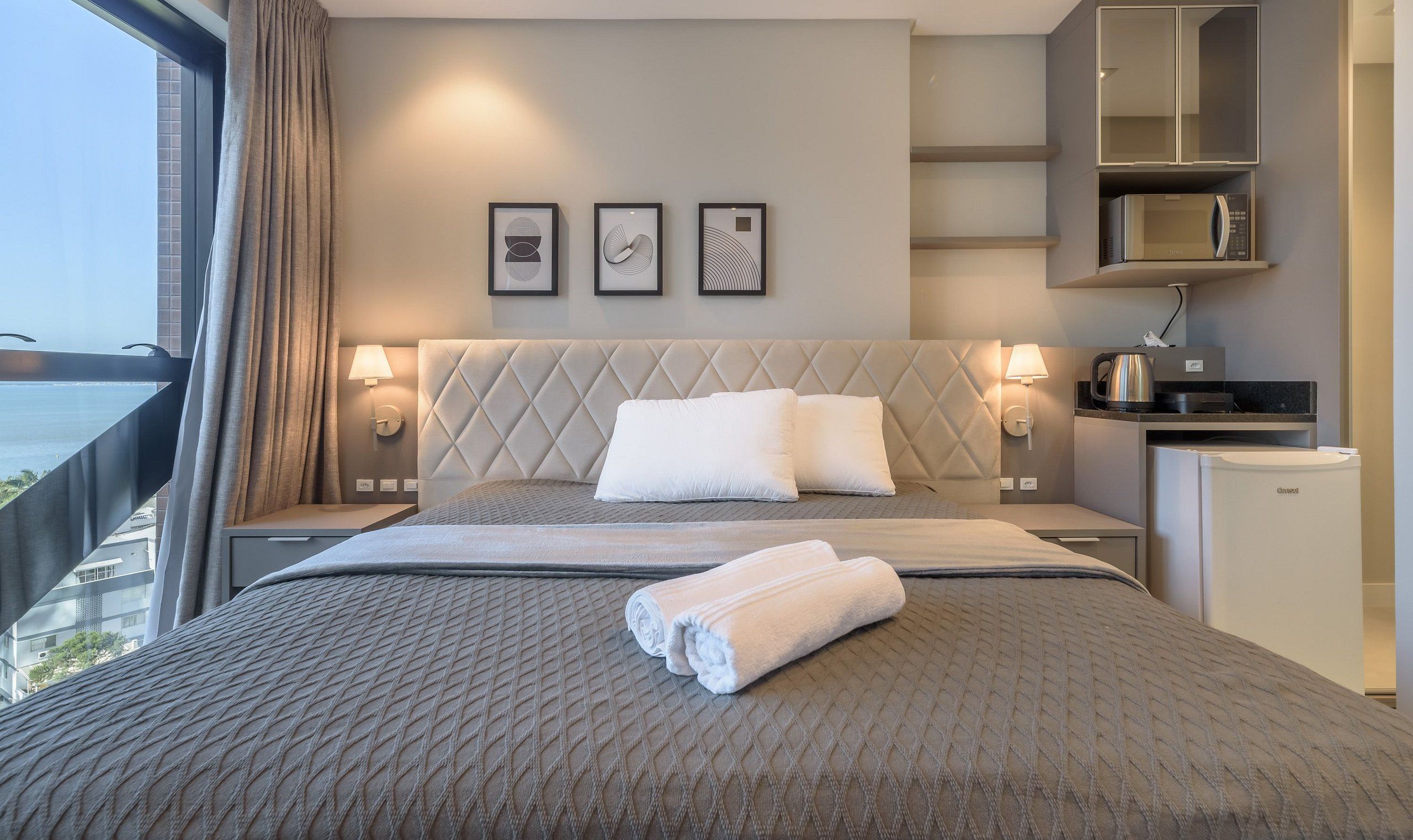 Una habitación de hotel con cama, escritorio, hervidor de agua y vista al mar.