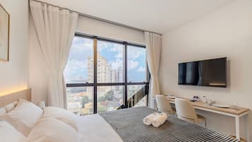 Habitación de hotel con un ventanal grande, cama, escritorio, silla y televisión de pantalla plana.