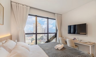 Habitación de hotel con un ventanal grande, cama, escritorio, silla y televisión de pantalla plana.