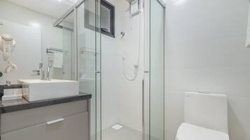 A modern bathroom with a glass shower enclosure, a white toilet, and a vanity with a mirror and towel rack.