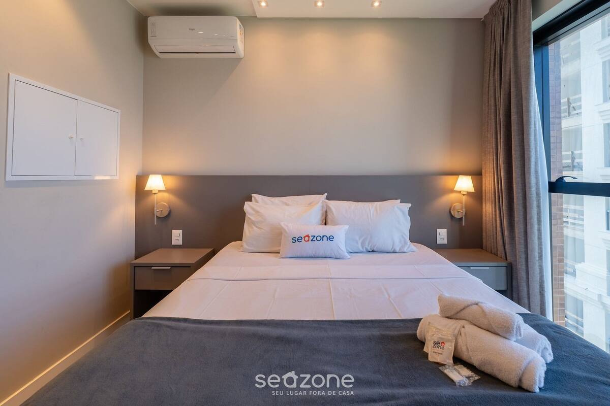 Une chambre d’hôtel comprenant un lit, deux lampes de chevet, une table de chevet, un appareil de climatisation et une fenêtre avec des rideaux.