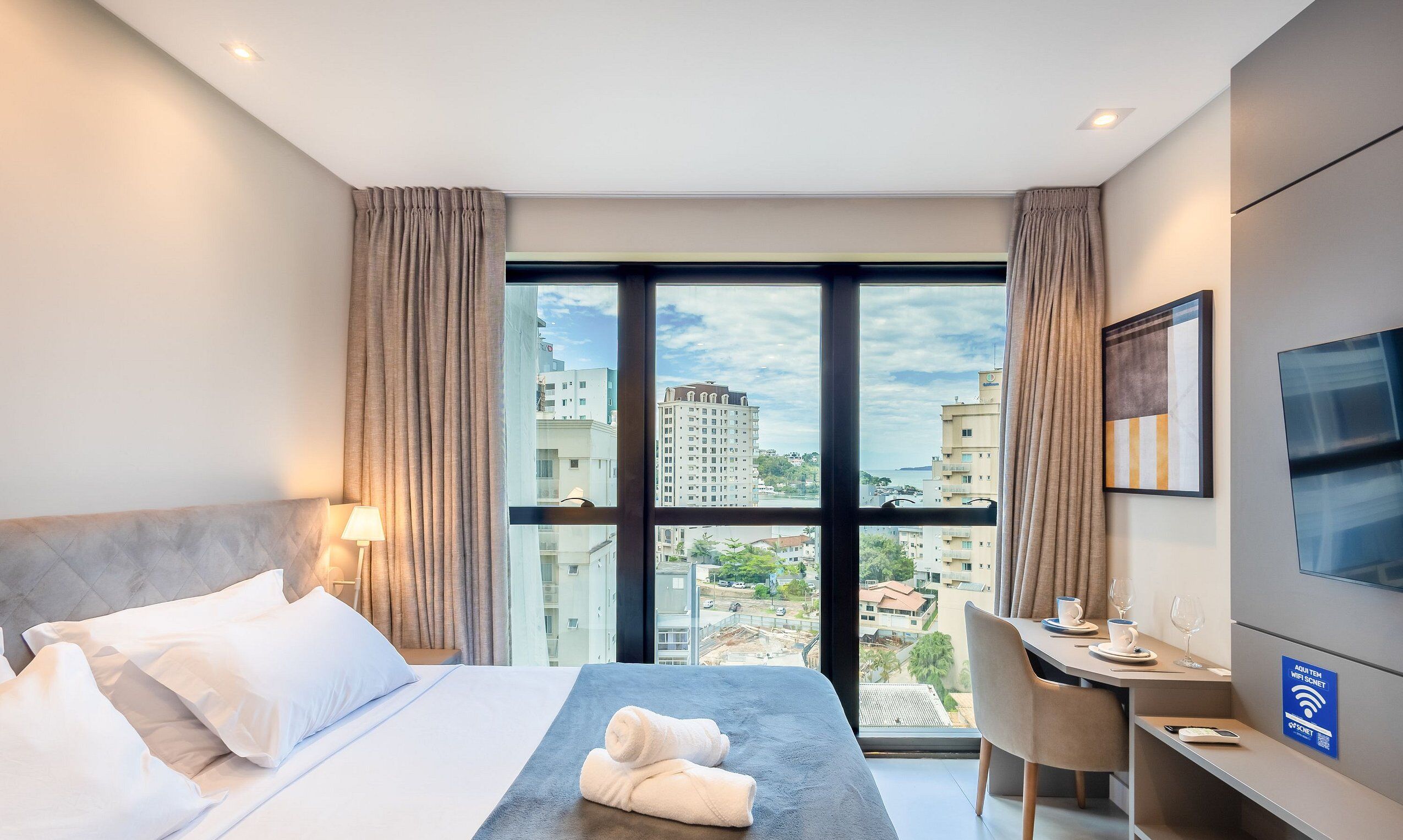 Une chambre d’hôtel avec un lit, un bureau, une chaise, une télévision et une vue sur la ville.