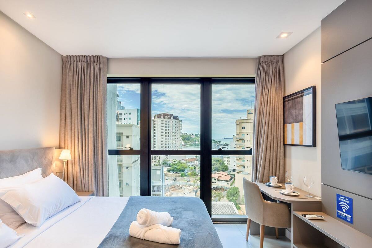 Une chambre d’hôtel avec un lit, un bureau, une chaise, une télévision et une vue sur la ville.