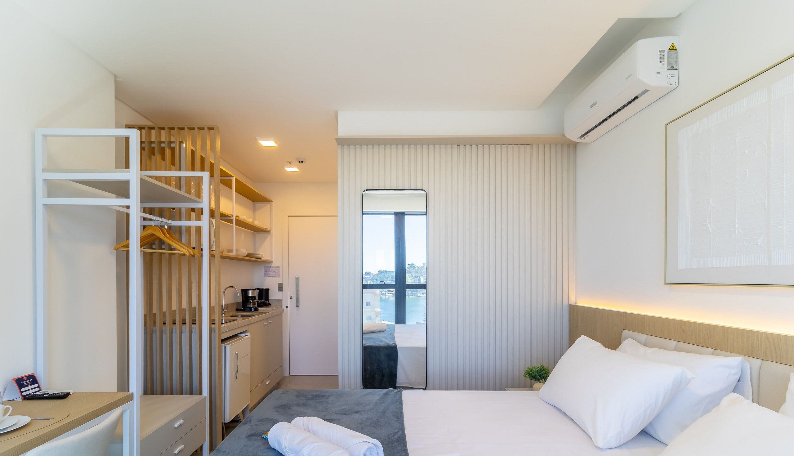 Habitación de hotel con cama, escritorio, kitchenette, armario y vistas a la ciudad.