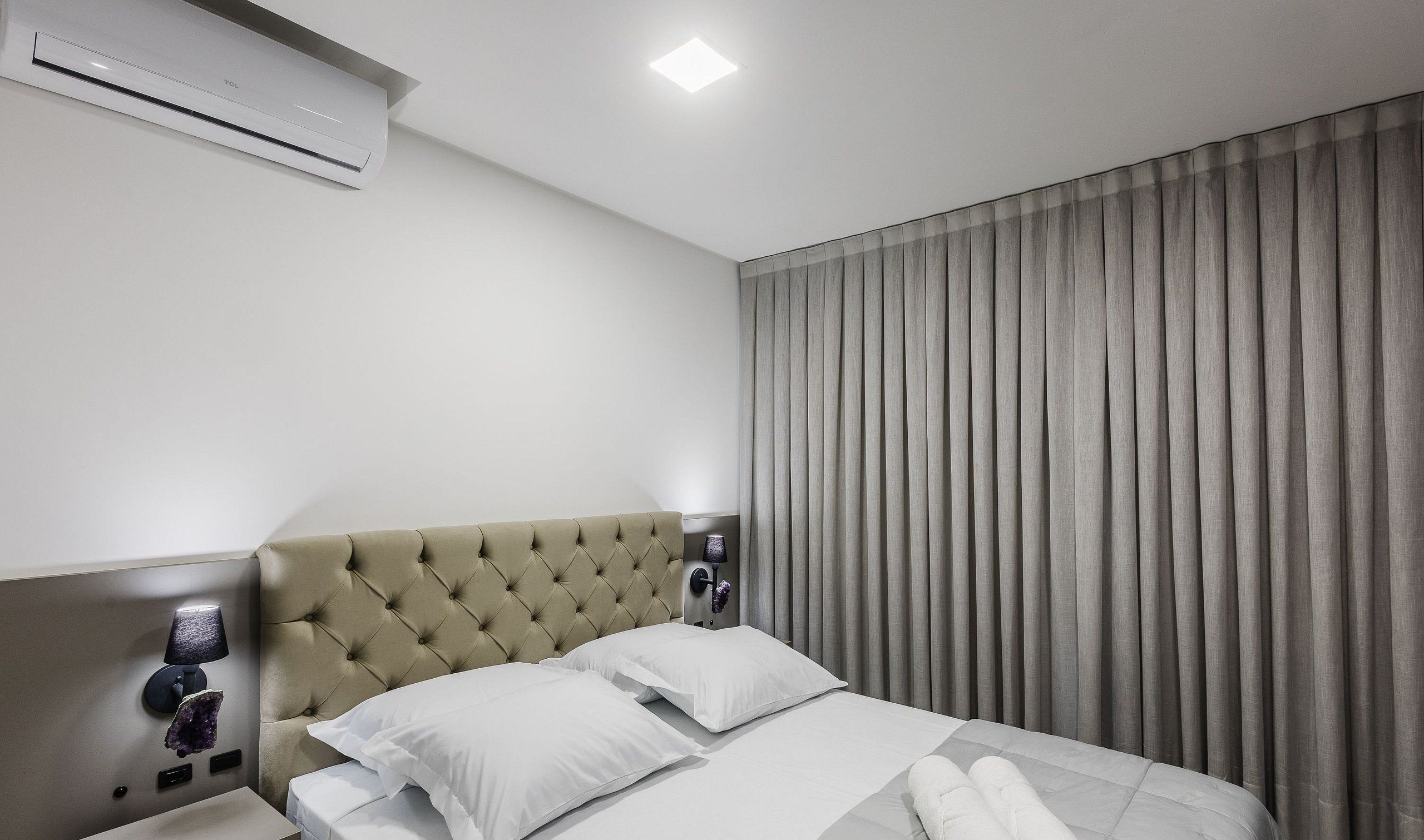 Une chambre d’hôtel comprenant un lit, une tête de lit, une table de chevet, un appareil de climatisation et un rideau.
