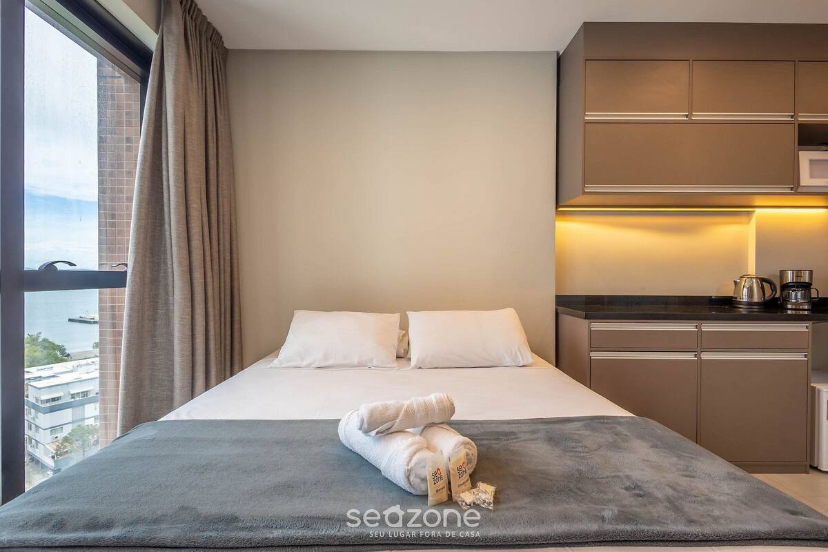 Une chambre d’hôtel avec un lit, une vue sur la ville, une kitchenette et une fenêtre avec des rideaux.