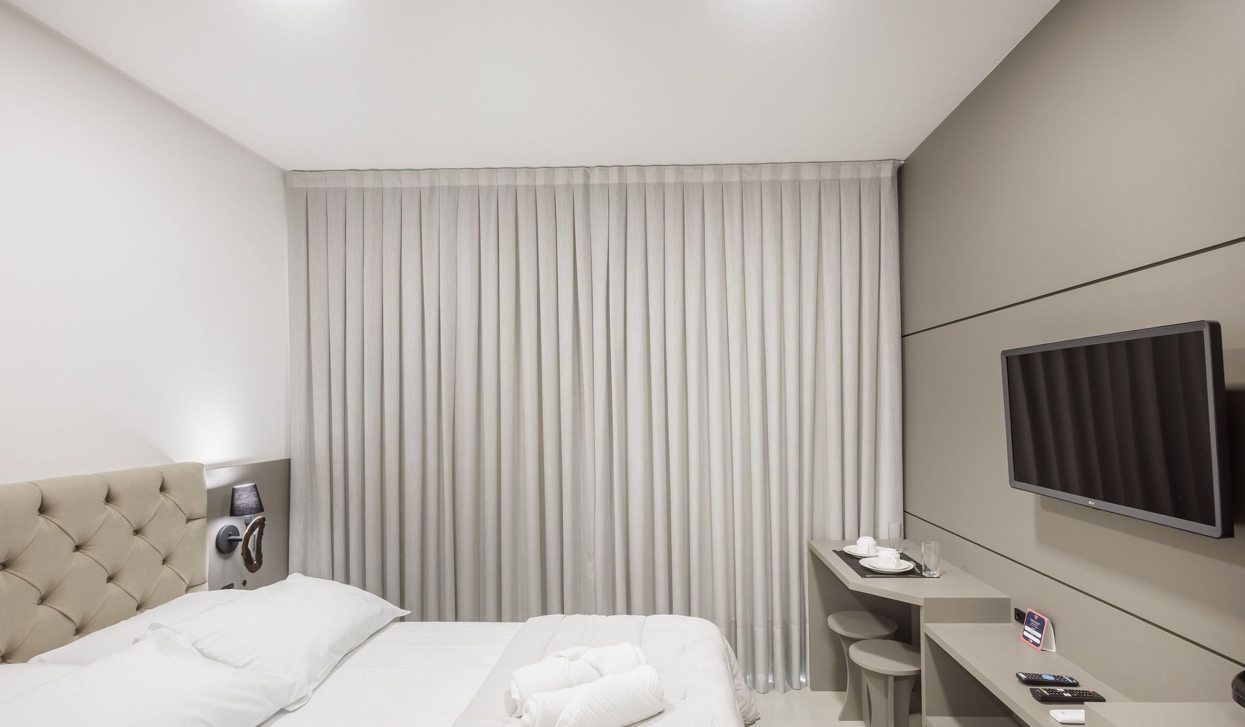 Une chambre d’hôtel avec un lit, un bureau, une télévision et une fenêtre avec des rideaux.