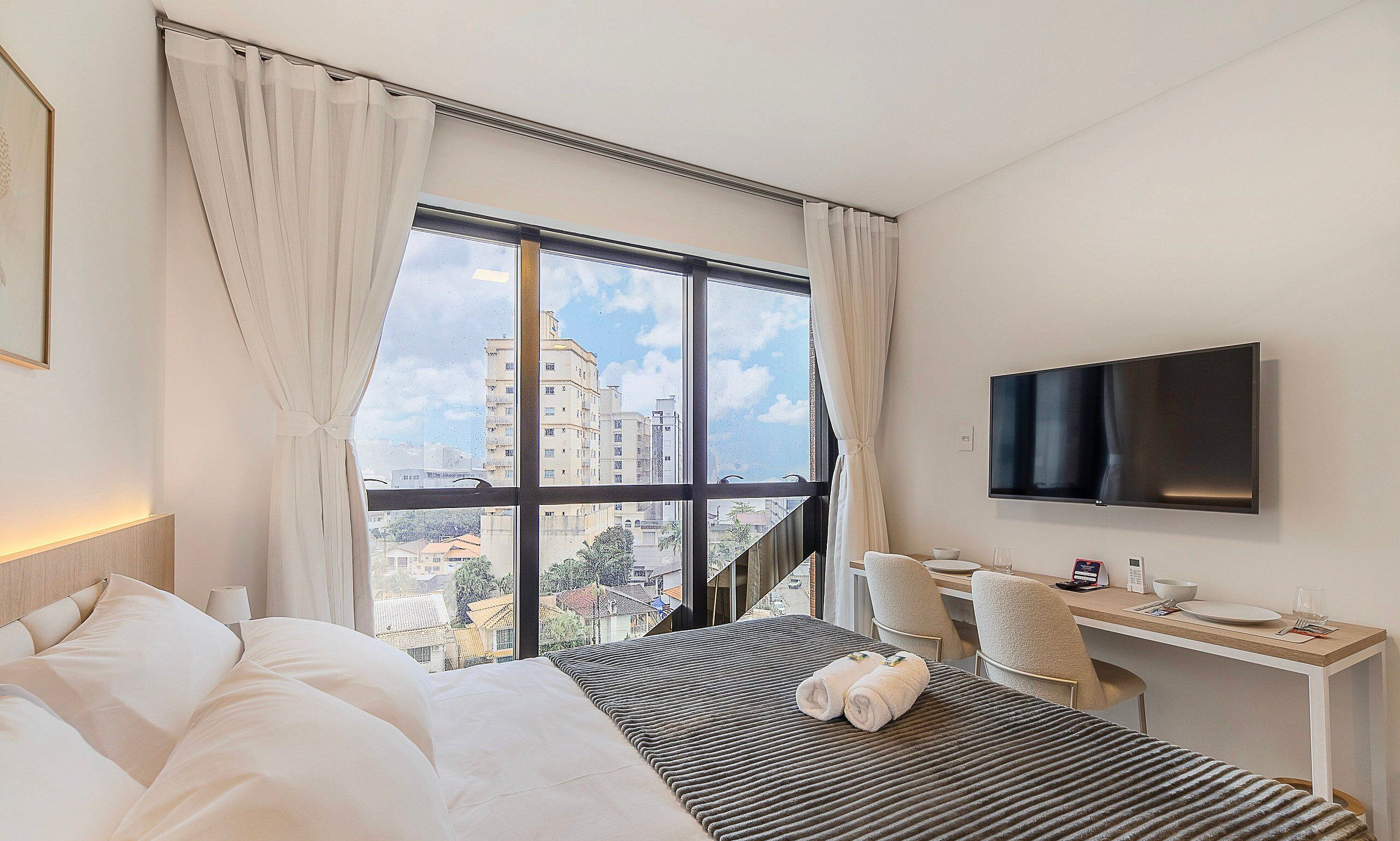 Une chambre d’hôtel avec un lit, un bureau, une télévision et une vue sur les bâtiments.