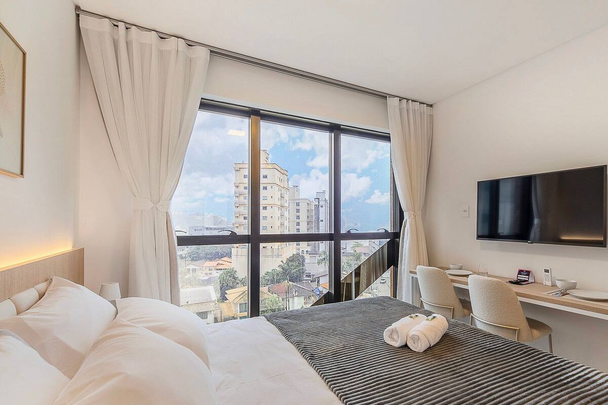 Une chambre d’hôtel avec un lit, un bureau, une télévision et une vue sur les bâtiments.