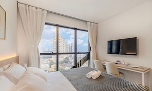 Quarto de hotel com cama, escrivaninha, televisão e vista para prédios.