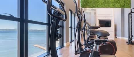A gym with exercise equipment, large windows, and a view of the sea.