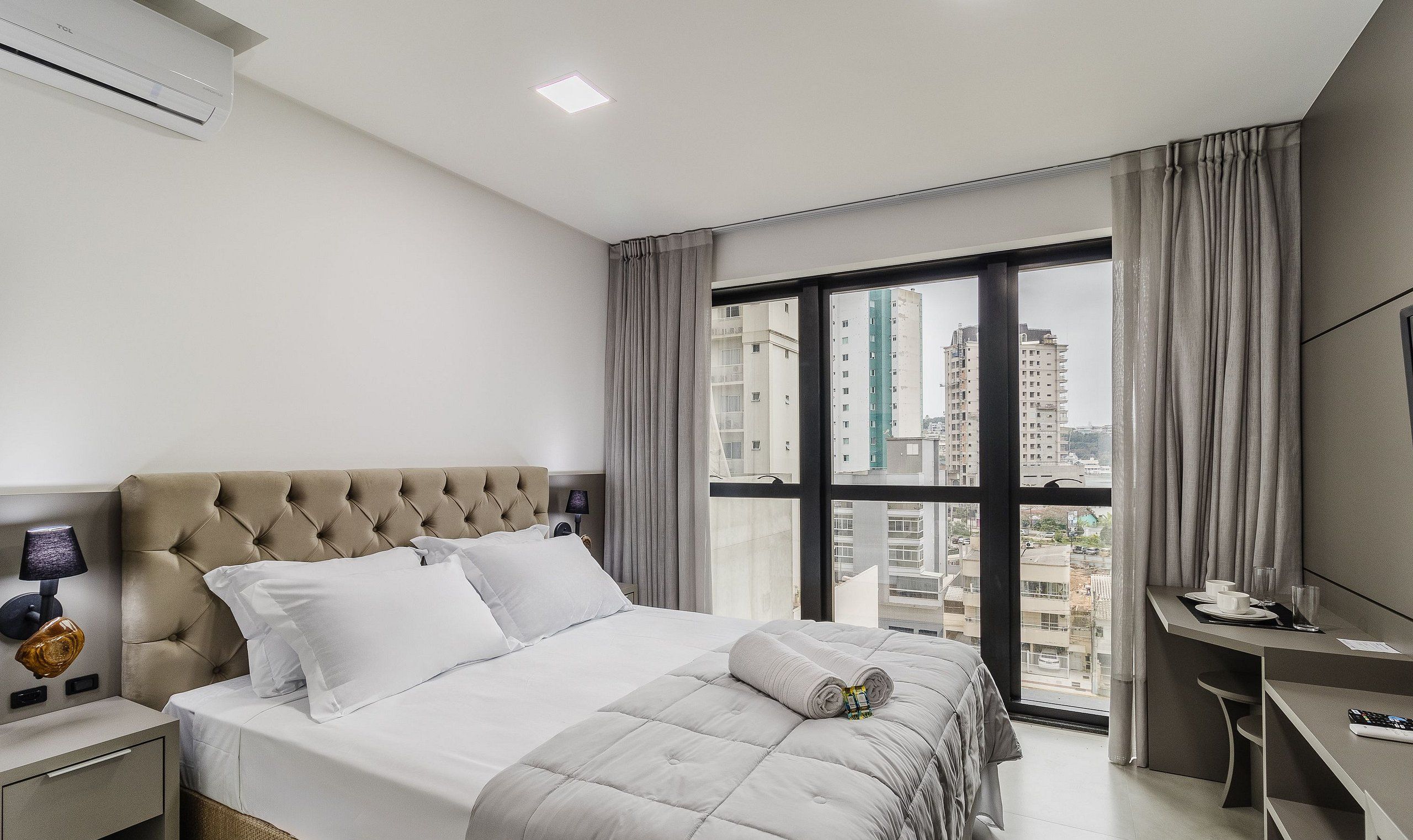 A modern hotel room with a large bed, a desk, and a view of the cityscape.