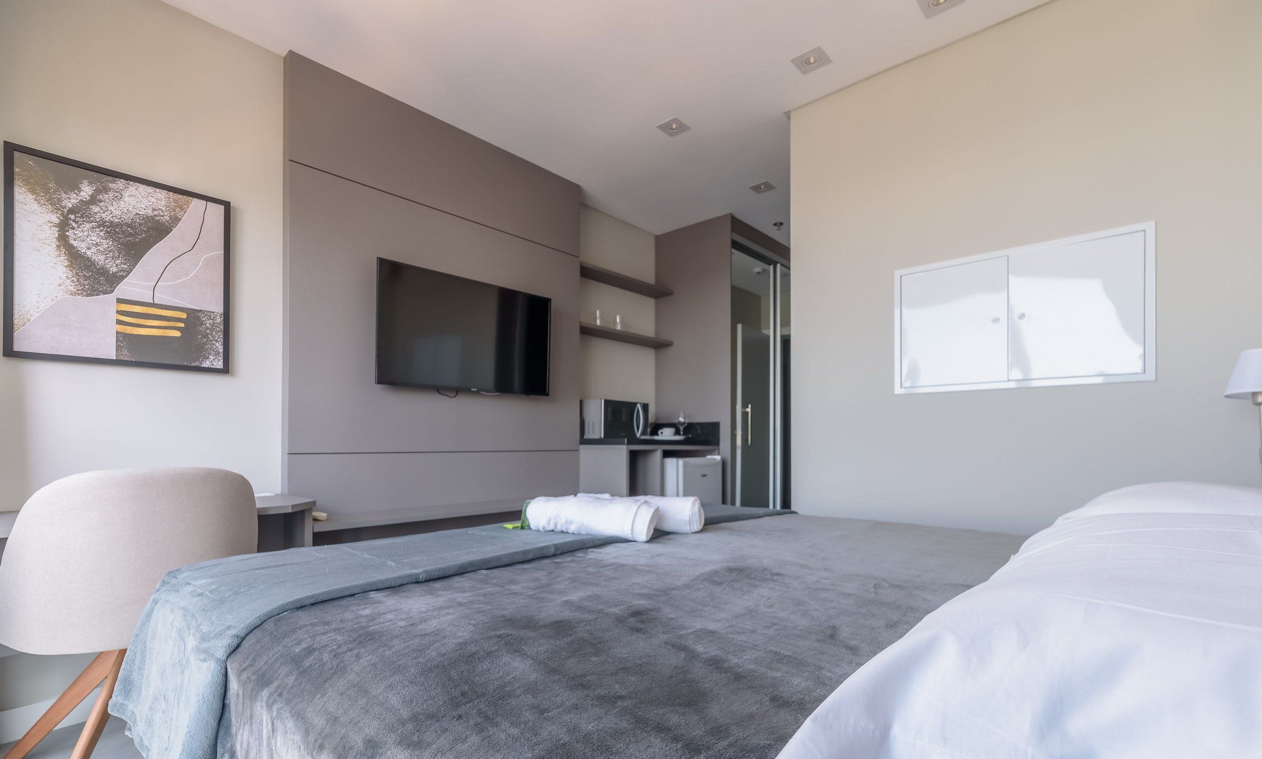 Habitación de hotel moderna con una cama, televisión, escritorio y baño visible a través de una puerta abierta.