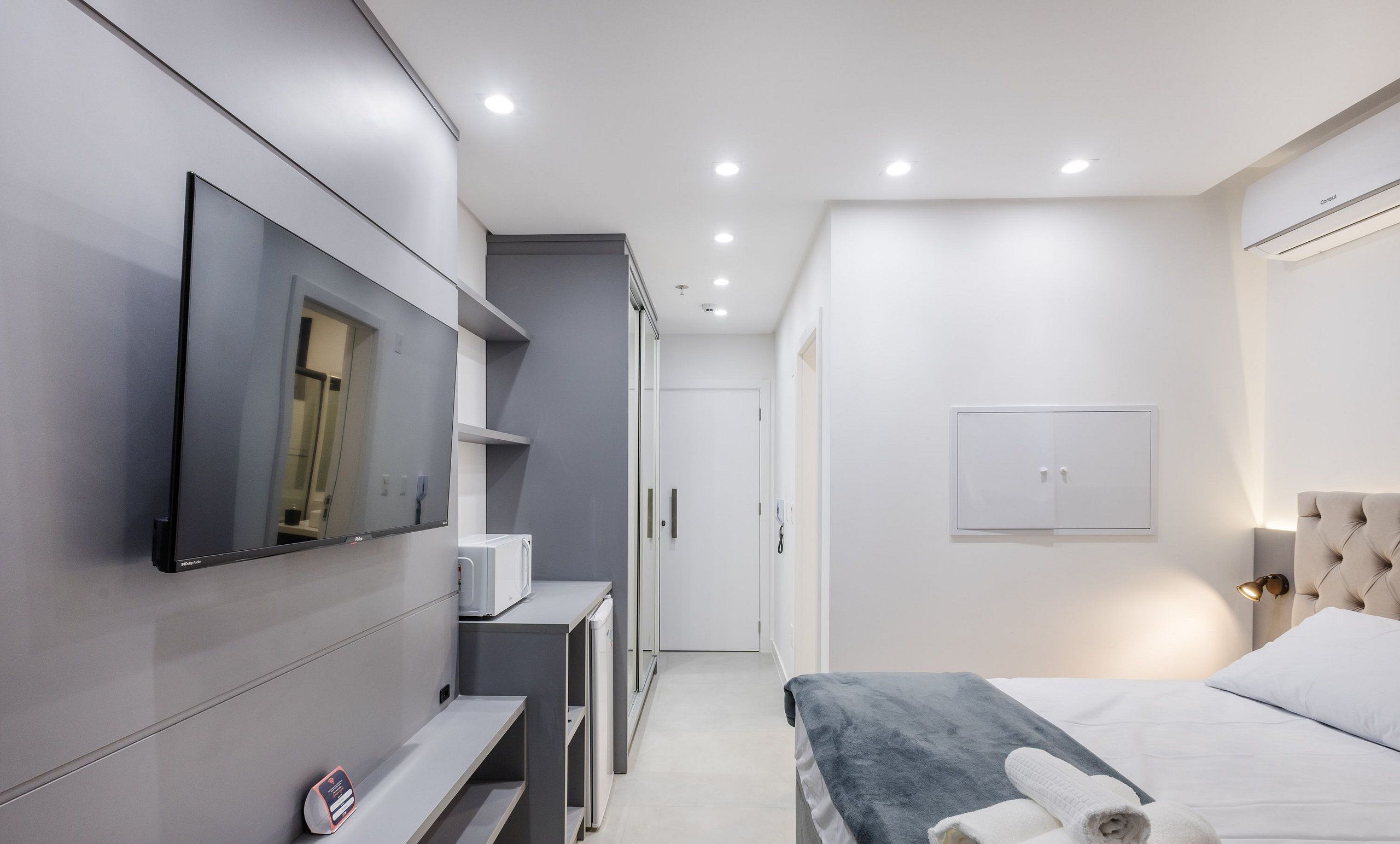 A modern bedroom with a bed, bedside table, and a television mounted on the wall.