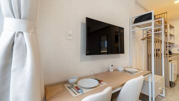 A modern hotel room with a dining area, a flat-screen TV mounted on the wall, and a walk-in closet with a hanging rod.