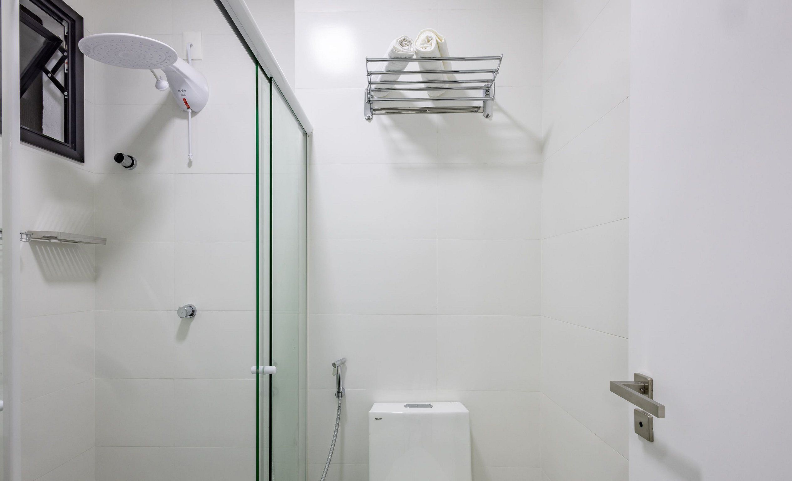 A modern bathroom with a glass shower enclosure, a white toilet, and a towel rack with towels.