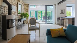 Un salon avec un mur en pierre, un canapé, un fauteuil, une table et une cheminée.