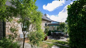 Un bâtiment en pierre doté d’un patio, d’un espace extérieur aménagé avec des sièges et d’une véranda en verre.
