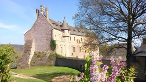 Un bâtiment historique doté d’une tour en pierre, d’une grande pelouse et de plantes en fleurs.