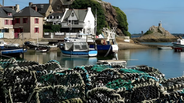 Un port où l’on peut voir des bateaux, des filets de pêche et des bâtiments aux volets rouges.