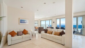 Amplia sala de estar con dos sofás blancos, una mesa de centro y un gran ventanal con vistas al mar.