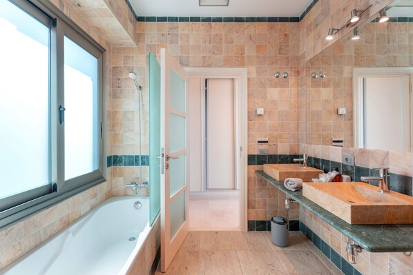 A modern bathroom with a bathtub, two sinks, and a large mirror.