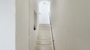 Un escalier étroit aux murs blancs mène à un palier où se trouve un luminaire.