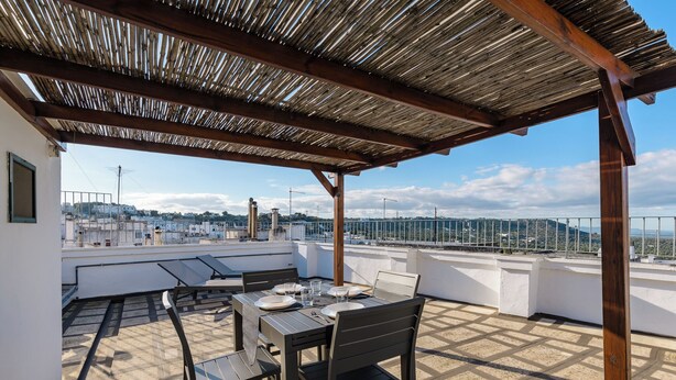 Une terrasse sur le toit, avec une table dressée pour le dîner, une pergola au-dessus et une vue panoramique sur la ville.