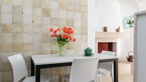Un coin repas avec un mur recouvert de carreaux, une table avec des chaises, un vase de fleurs et une cheminée.