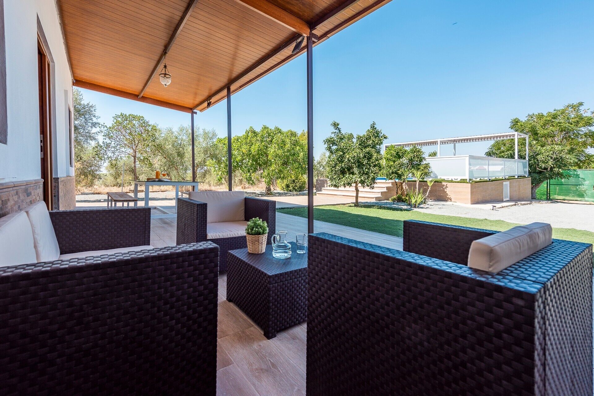 An outdoor patio with wicker furniture, a pergola, and a view of a landscaped area.