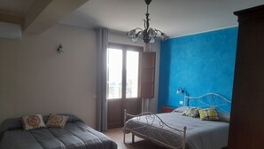 A bedroom with two beds, a chandelier, a window with curtains, and a blue accent wall. - Arcobaleno dell'Etna - Family Room with terrace and Etna-sea view (Calatabiano)