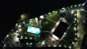 An aerial view of a hotel with a swimming pool, outdoor seating area, and well-lit pathways.