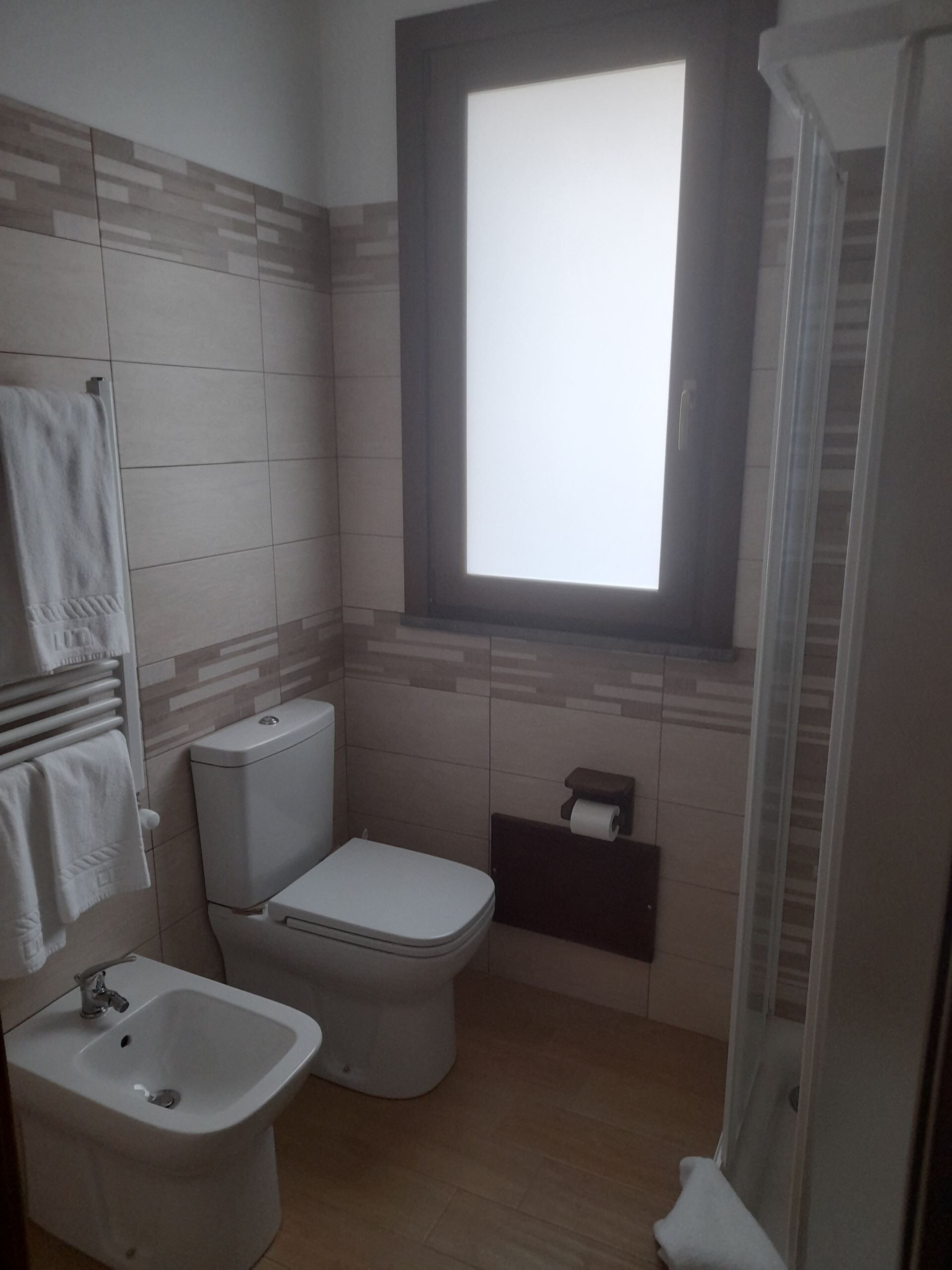 A small bathroom with a toilet, bidet, and a window.