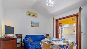 Un comedor con una mesa preparada para cuatro, un sofá azul, un mueble de madera y un aire acondicionado de pared.
