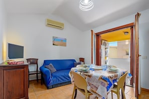 Un coin repas avec une table dressée pour quatre personnes, un canapé bleu, un meuble en bois et un climatiseur fixé au mur.