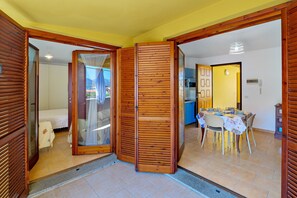 Une pièce comprenant un lit, une porte coulissante en bois, un coin repas avec une table et des chaises, et une cuisine à l’arrière-plan.