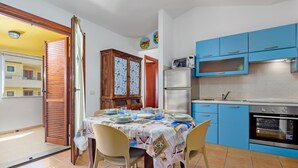 Un comedor con una mesa preparada para cuatro personas, una cocina con armarios azules, un refrigerador y un horno.