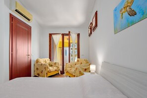 Une chambre d’hôtel avec un lit, deux chaises, une porte, un climatiseur, un tableau et une fenêtre avec des rideaux.