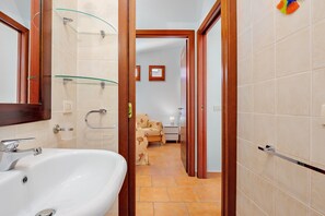 Une salle de bain avec un lavabo blanc, des étagères en verre et un espace douche.