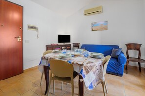Ein Essbereich mit einem Tisch für vier Personen, einem blauen Sofa, einem Holzstuhl, einem Fernseher und einer wandmontierten Klimaanlage.