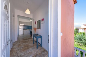 Un couloir mène à une cuisine qui comprend un coin repas, une table ornée d’un vase, et offre une vue sur la verdure à l’extérieur.