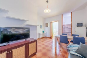 A living room with a TV, a dining area with chairs, a sofa, and a kitchen area with a fridge. - Portobello sul mare by Rentbeat (Villanova)