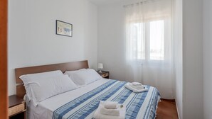 Una habitación de hotel con cama, mesita de noche, lámpara, ventana con cortinas y un cuadro en la pared.