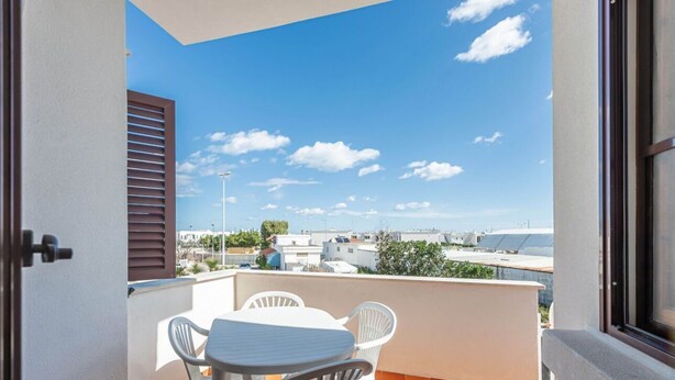 Un balcón con mesa y sillas, vista panorámica de la ciudad y cielo despejado.