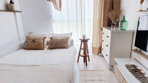 Un dormitorio con cama, mesita de noche, cómoda, televisor y objetos decorativos.