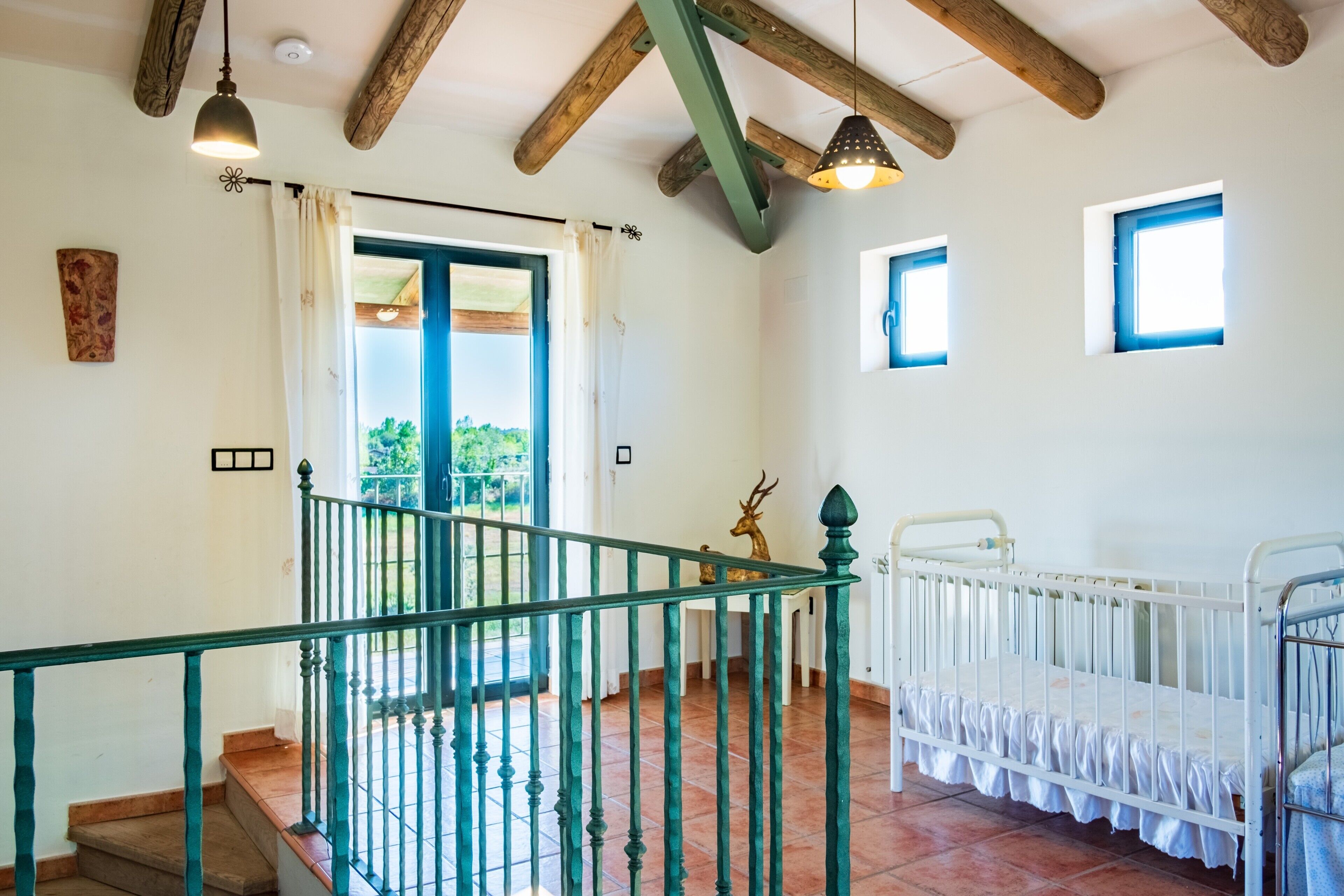A room with a staircase, a crib, a door leading outside, and a small window.